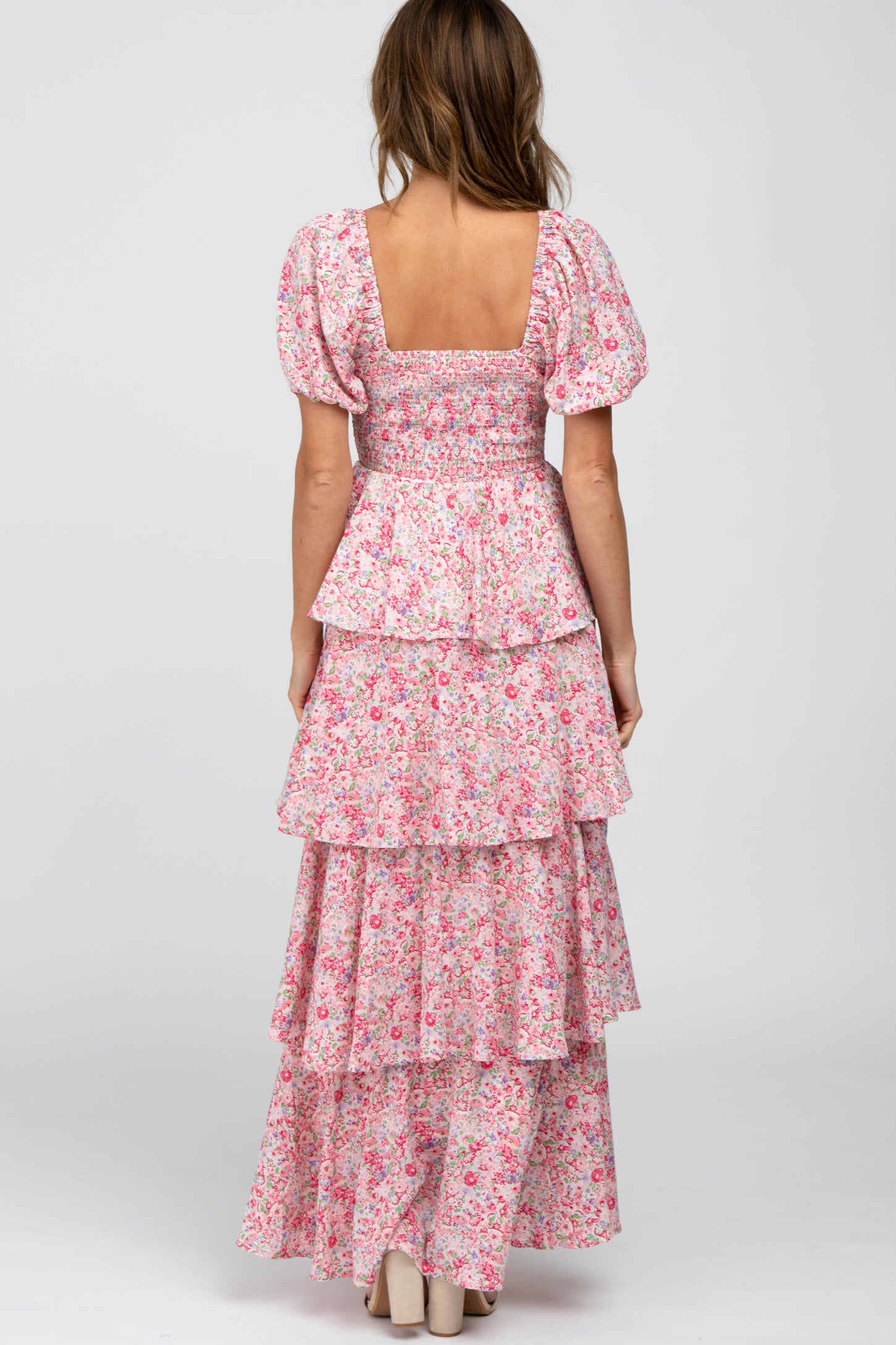 Back view of a woman wearing a pink floral tiered maxi dress with puff sleeves and a smocked bodice