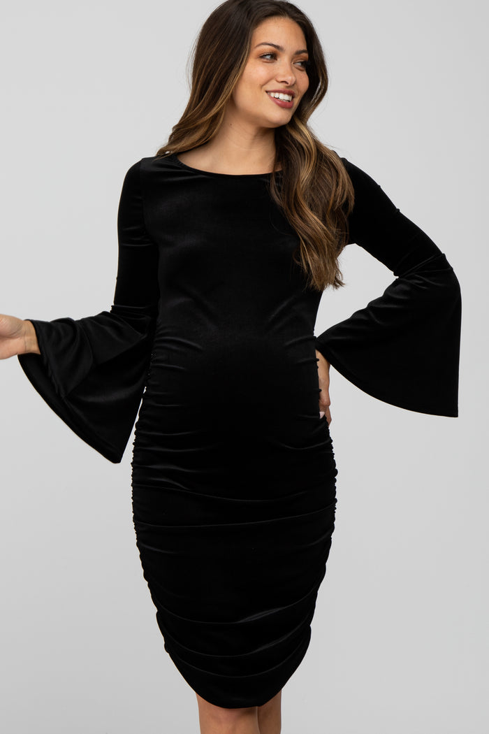 woman wearing a black velvet long sleeve maternity dress with bell sleeves and a visible baby bump