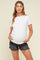 woman wearing a white short sleeve maternity top and showing her baby bump with black distressed denim shorts
