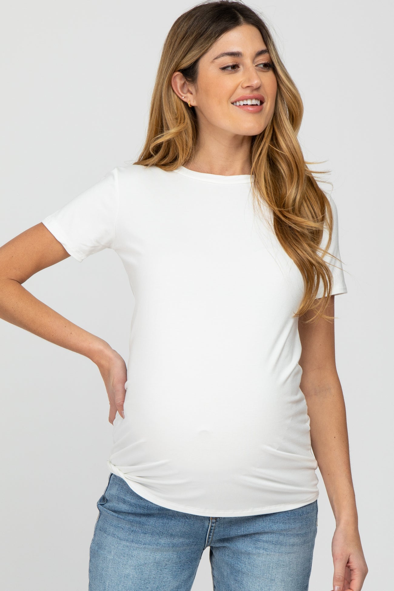 woman wearing a white short sleeve maternity top with a visible baby bump and styled with light blue jeans