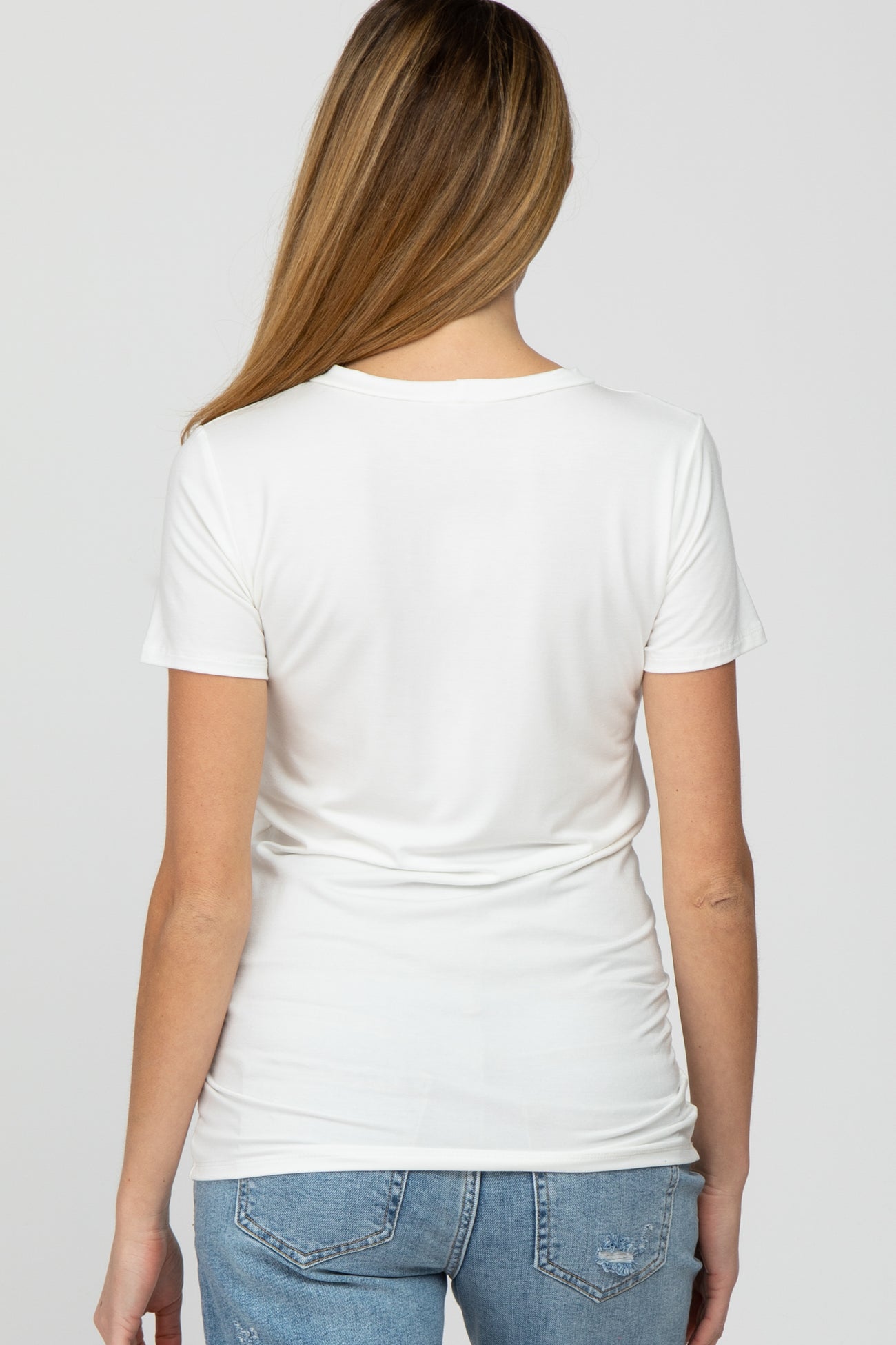 woman wearing a white short sleeve maternity top, viewed from the back, paired with blue denim jeans