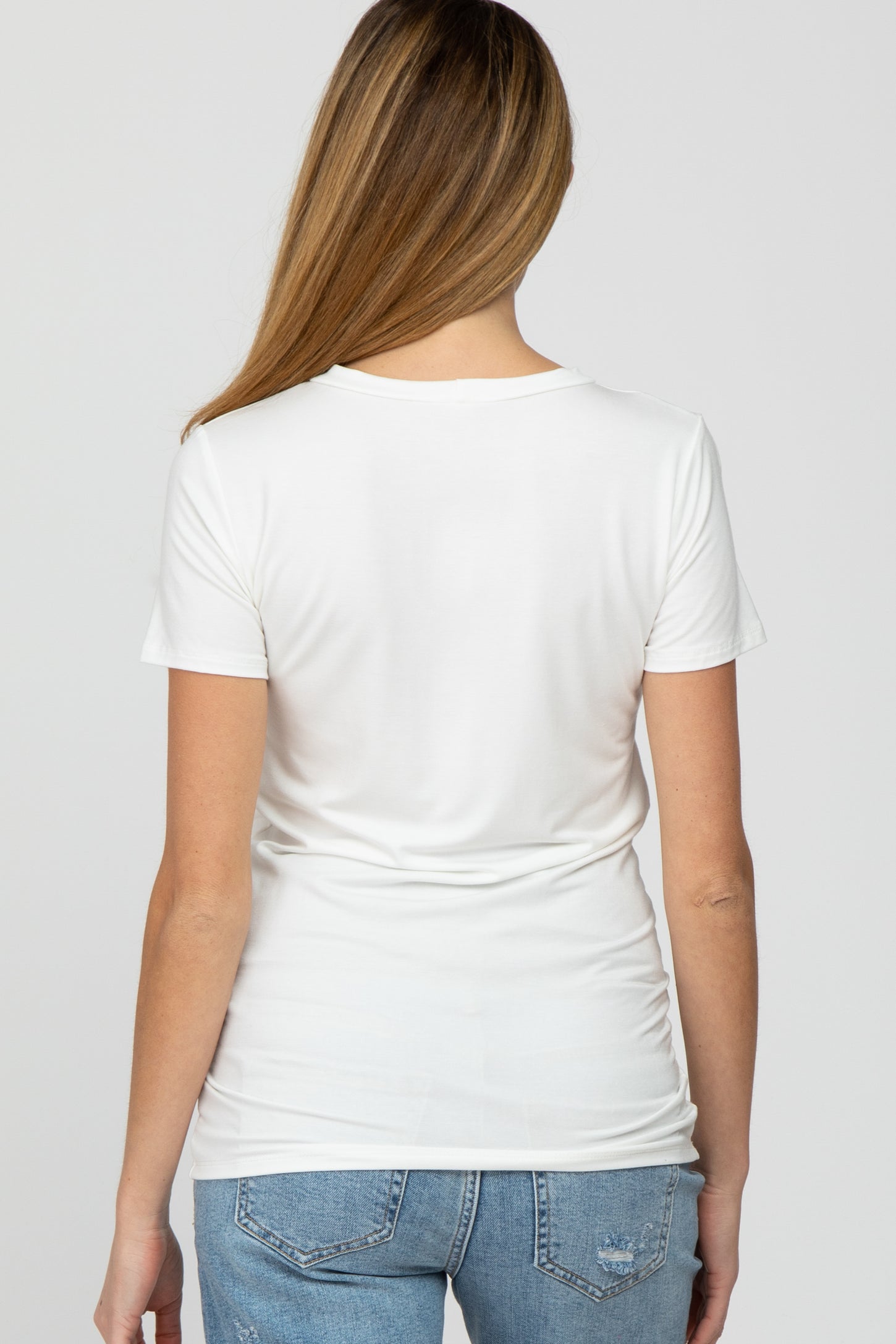 woman wearing a white short sleeve maternity top, viewed from the back, paired with blue denim jeans