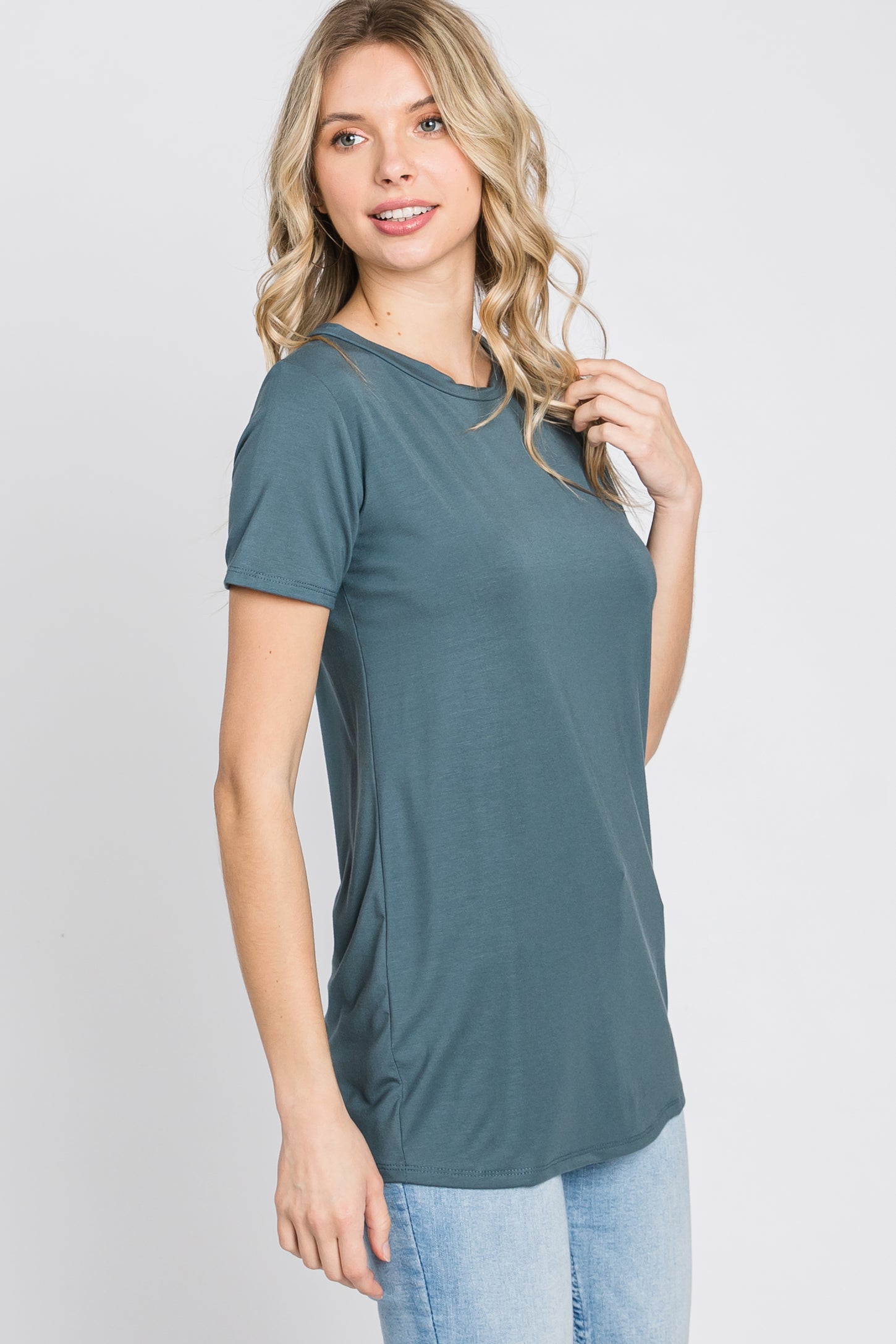 woman wearing a teal short sleeve top with side ruching and a relaxed fit, posing with hand on her shoulder