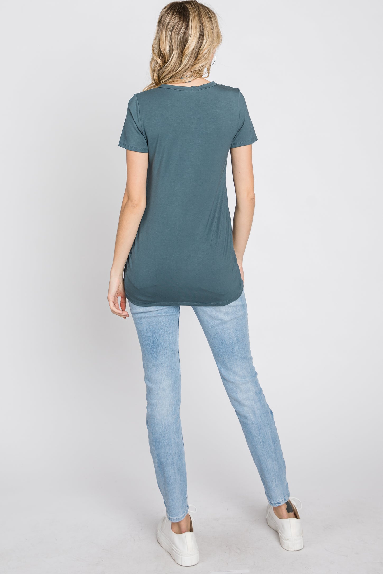 woman wearing a dark teal short sleeve top and light blue skinny jeans, viewed from the back