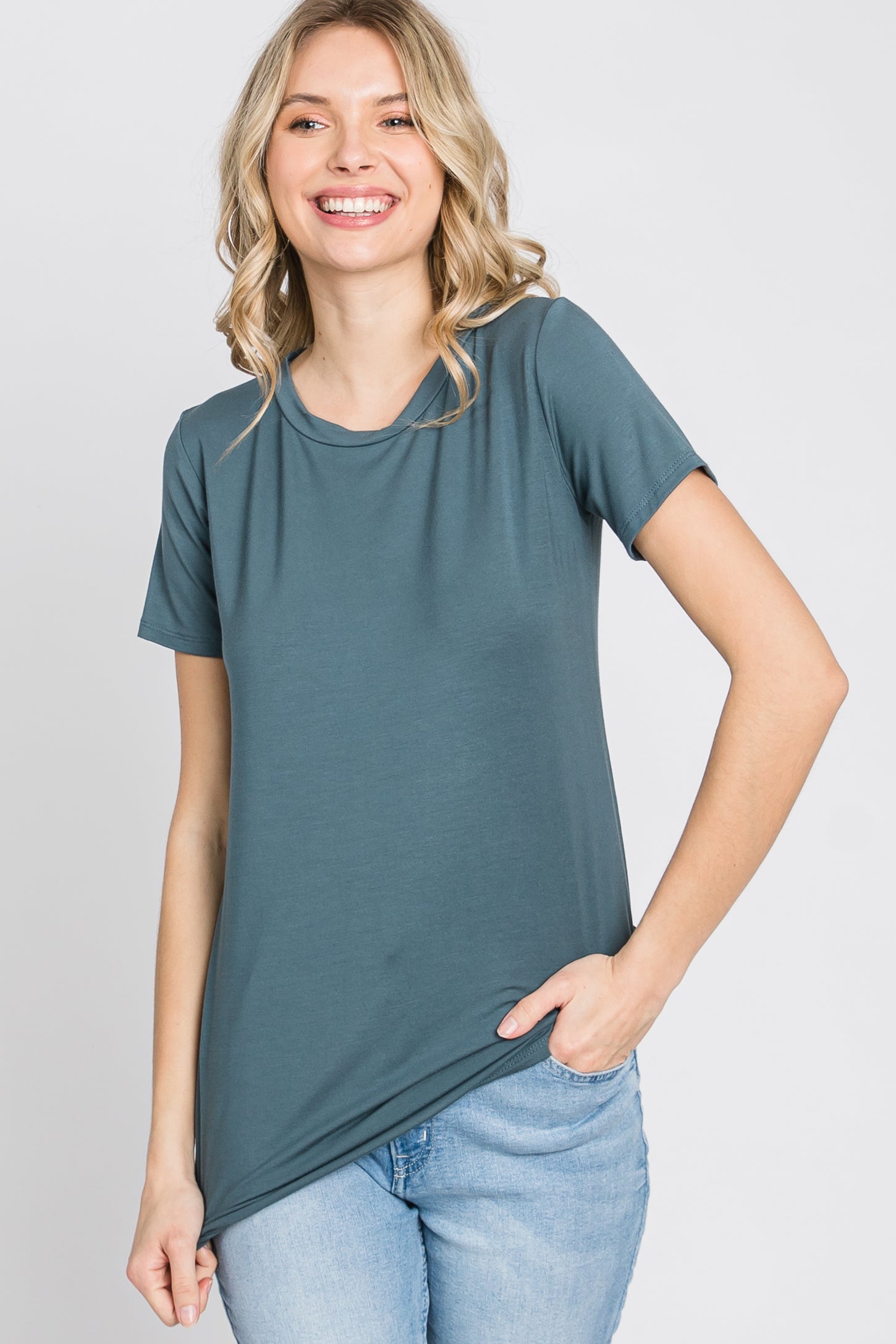 woman wearing a dark teal short sleeve t-shirt paired with light blue jeans and smiling at the camera
