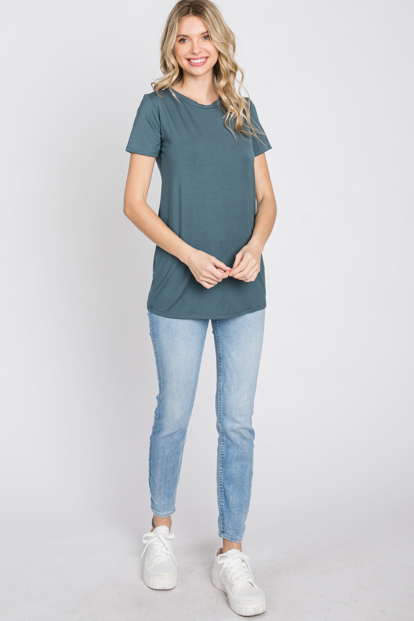 woman wearing a teal short sleeve top and light blue skinny jeans, standing and smiling