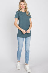 woman wearing a teal short sleeve top and light blue skinny jeans, standing and smiling