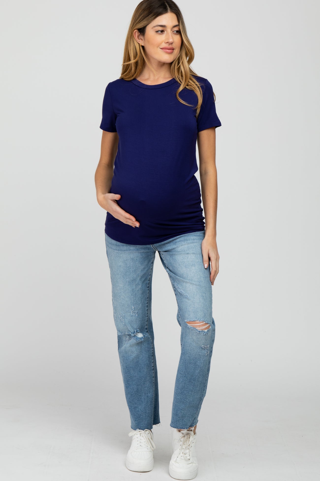 woman wearing a navy blue short sleeve maternity top and distressed light wash jeans, with her baby bump visible