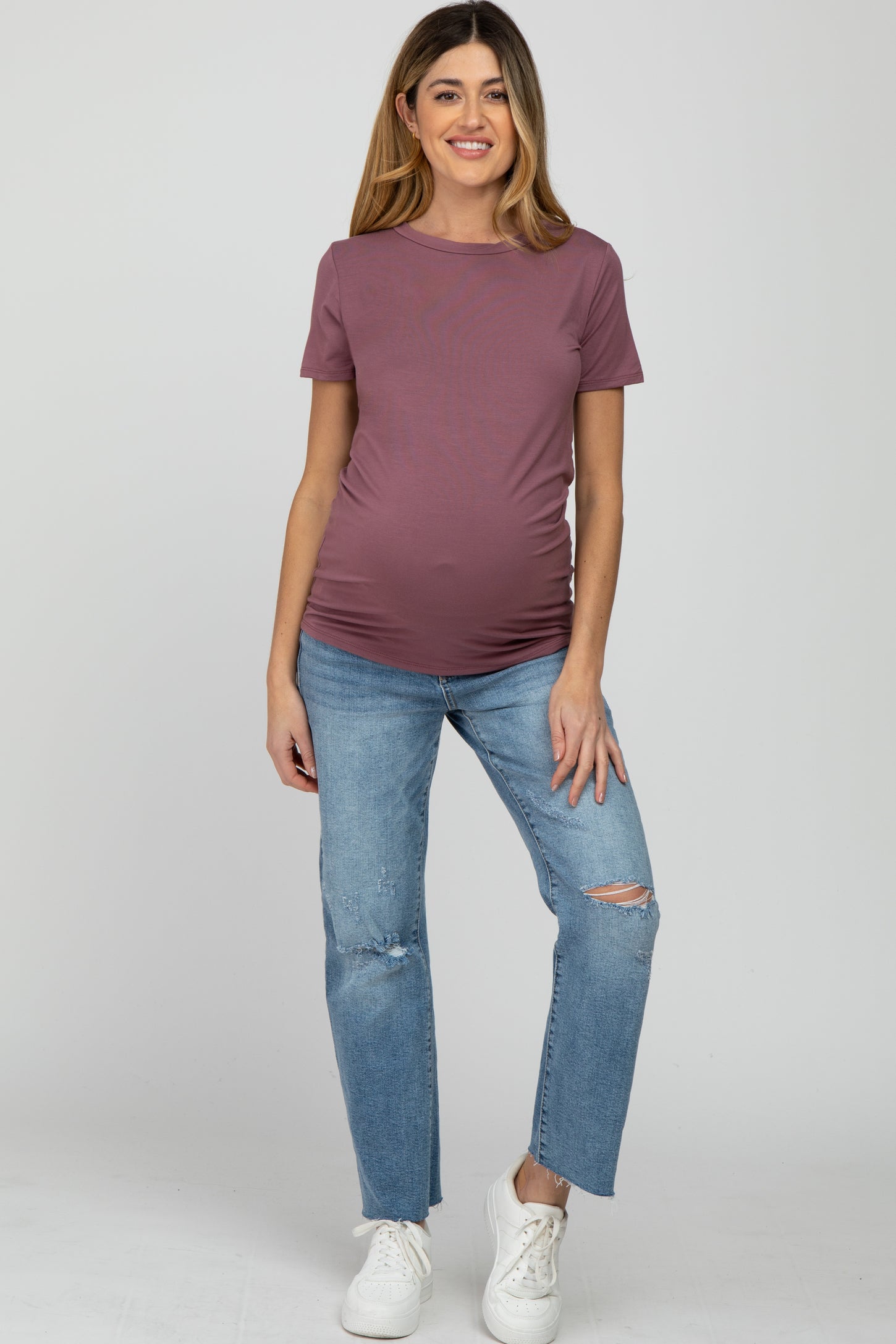 woman wearing a mauve short sleeve maternity top and distressed blue jeans, showing her baby bump