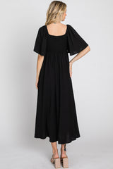 woman wearing a black smocked maxi dress with short flutter sleeves, shown from the back