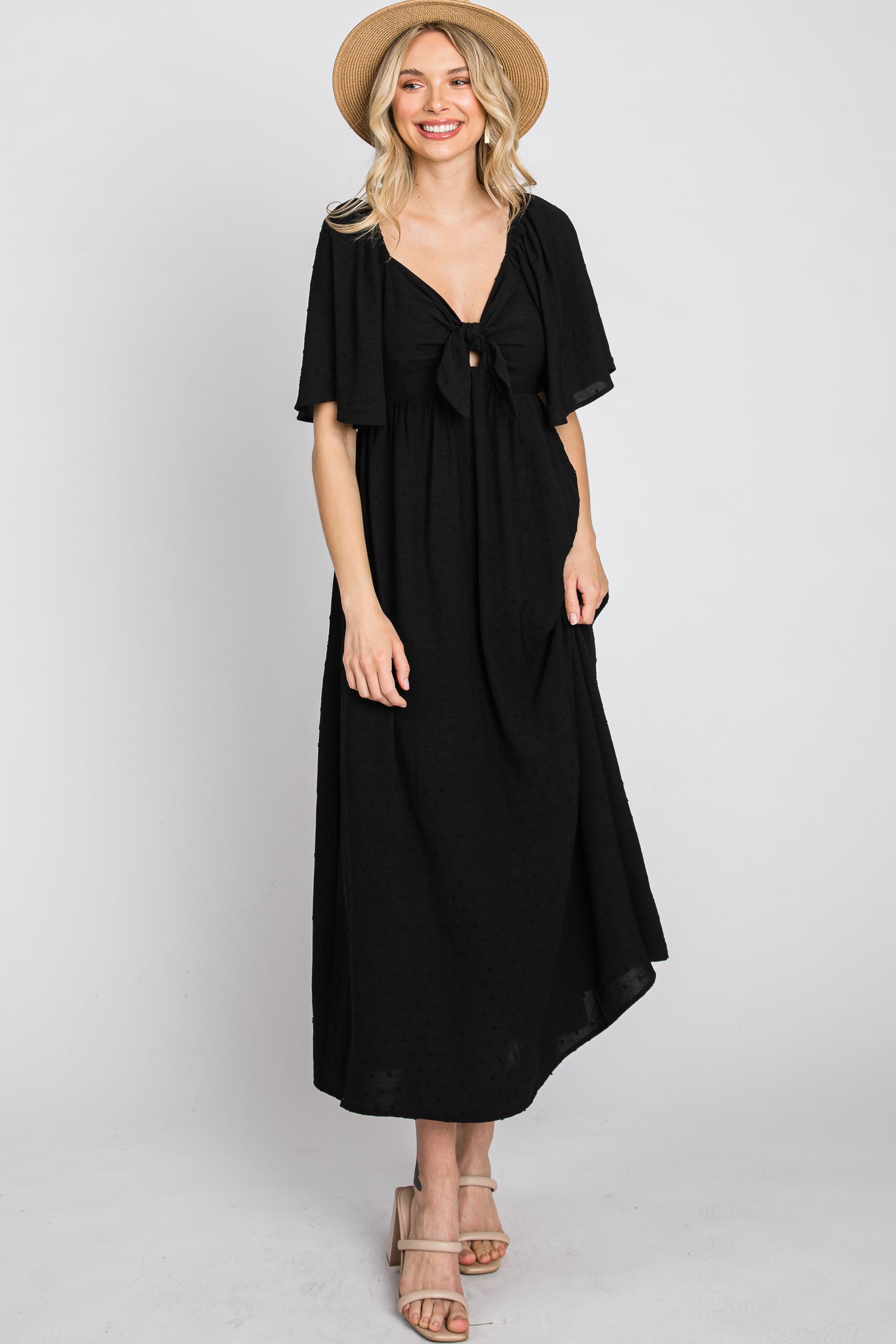 woman wearing a black maxi dress with short sleeves and a tie front detail, paired with a straw hat and sandals