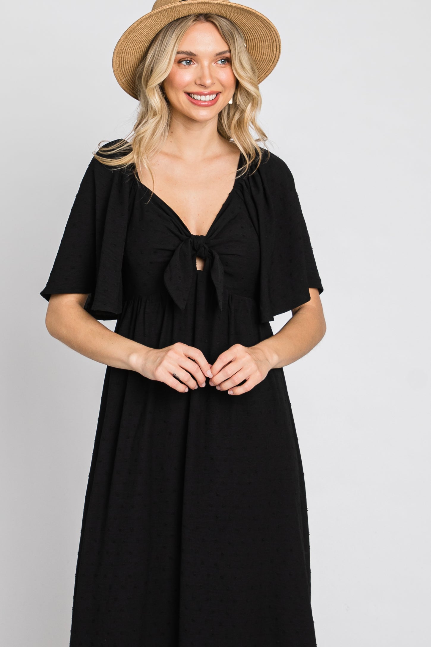 woman wearing a black maxi dress with flutter sleeves and a tie front detail, accessorized with a straw hat