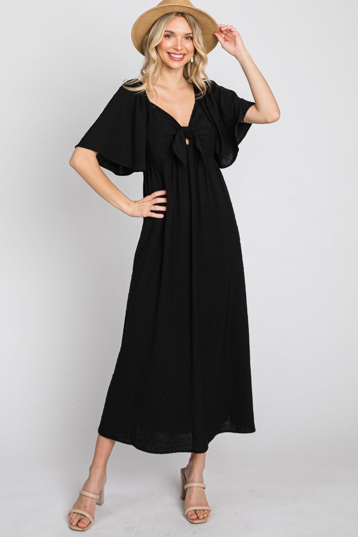woman wearing a black maxi dress with a front knot detail and flutter sleeves, styled with a straw hat and sandals