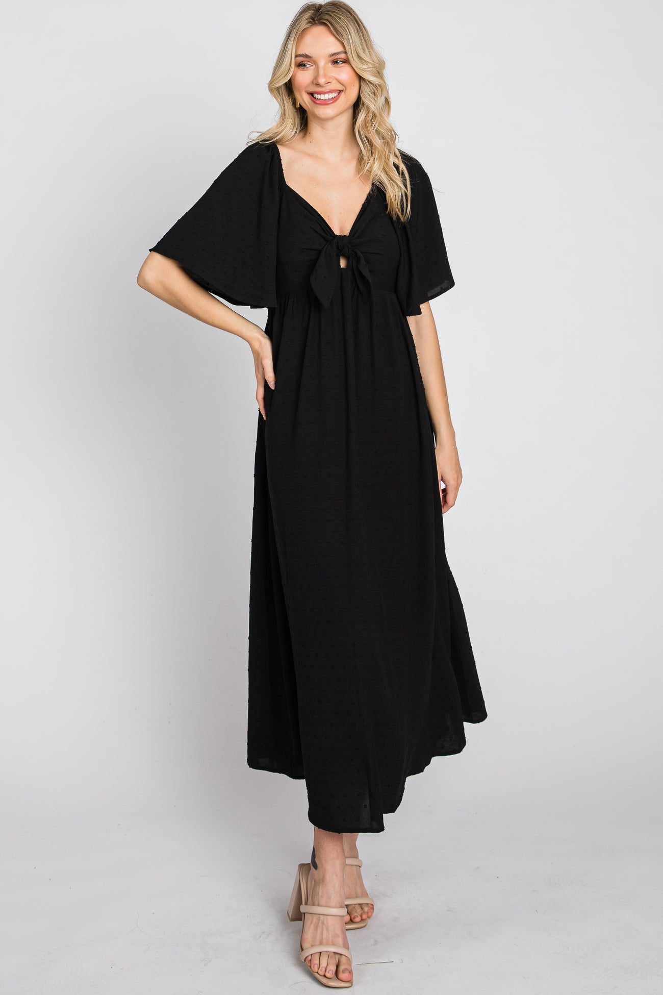 woman wearing a black maxi dress with a bow detail at the front and flared sleeves, standing and smiling