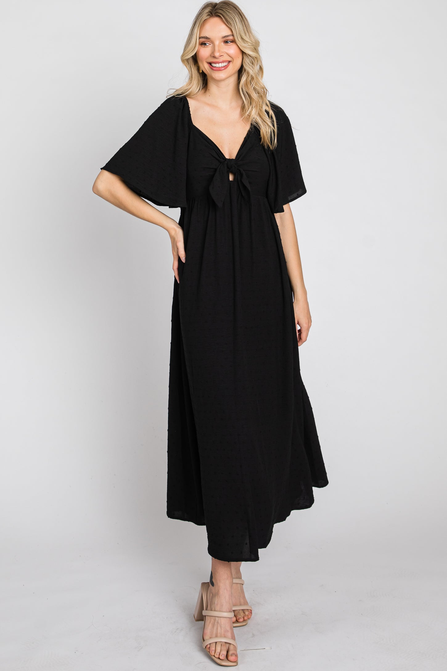 woman wearing a black maxi dress with a bow detail at the front and flared sleeves, standing and smiling