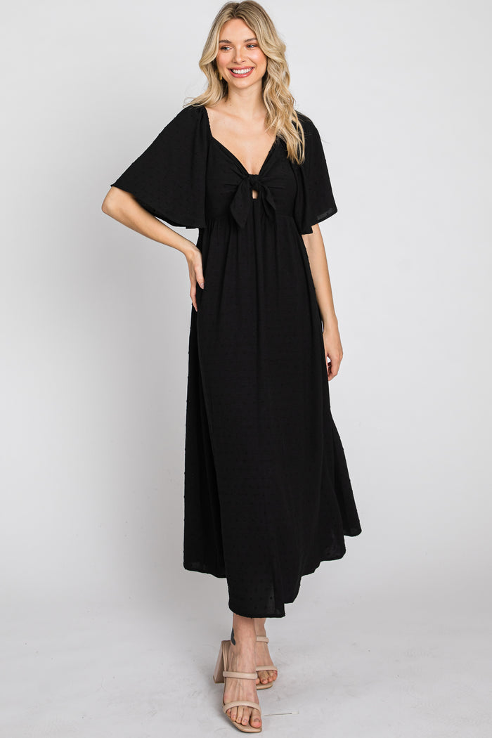 woman wearing a black maxi dress with a bow detail at the front and flared sleeves, standing and smiling