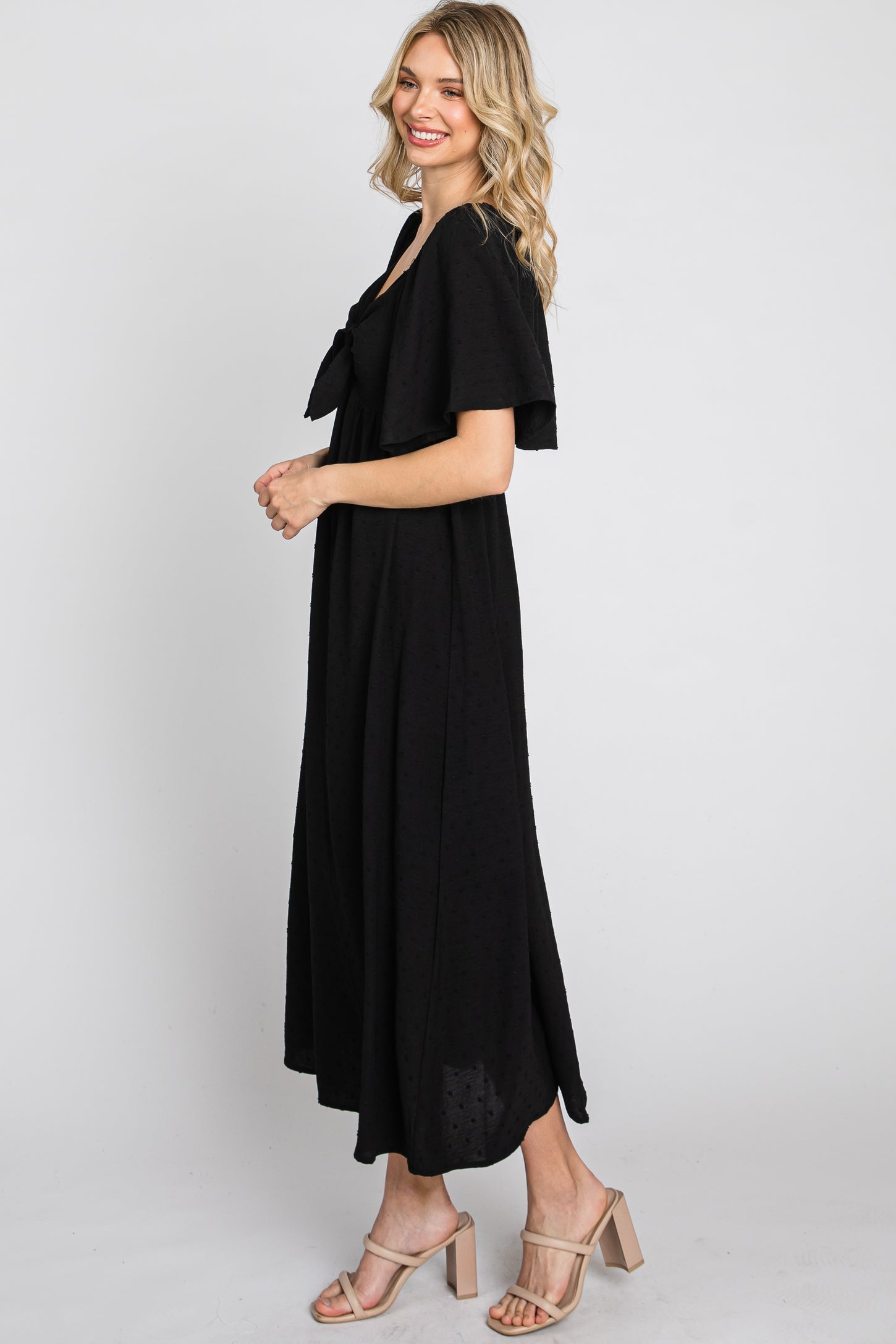 woman wearing a black midi dress with a bow detail and flutter sleeves, standing in profile against a plain background
