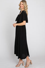 woman wearing a black midi dress with a bow detail and flutter sleeves, standing in profile against a plain background