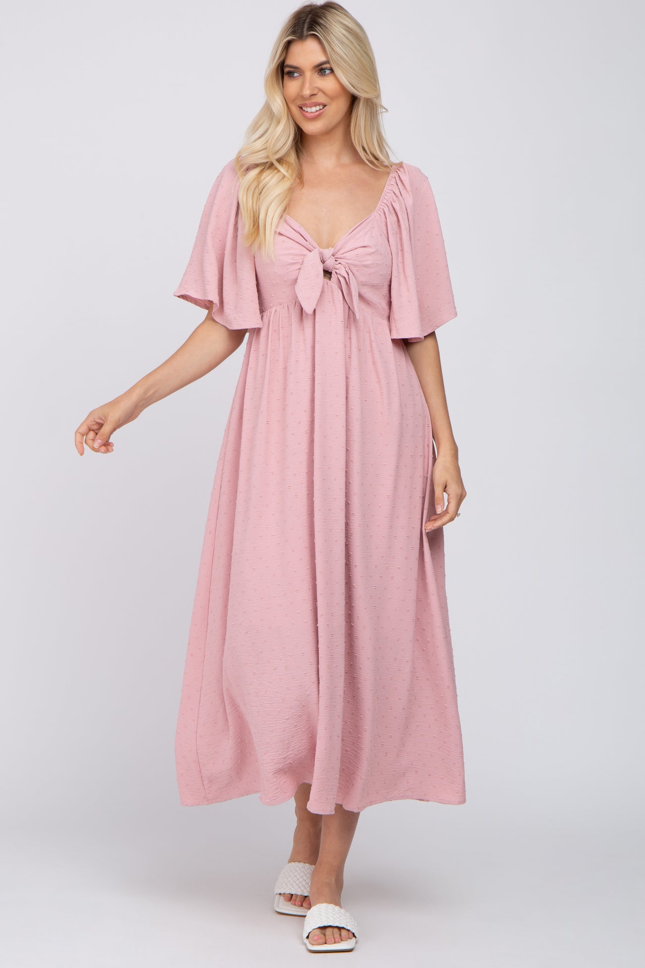 woman wearing a light pink maxi dress with flutter sleeves and a tie-front detail