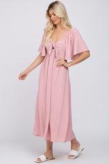 woman wearing a pink maxi dress with flutter sleeves and a front tie detail