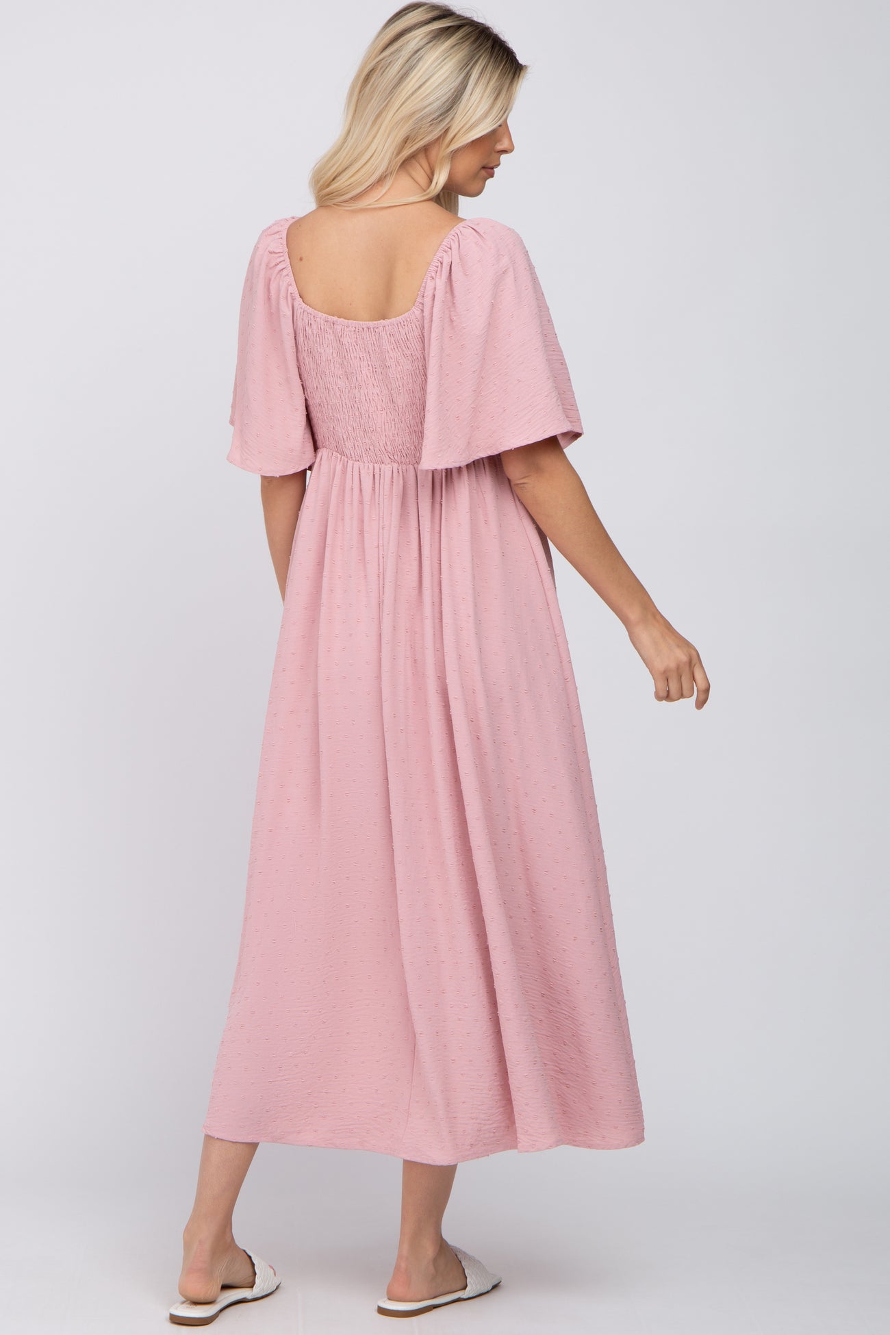 woman wearing a pink midi dress with short puff sleeves and a smocked back, standing sideways with a relaxed fit