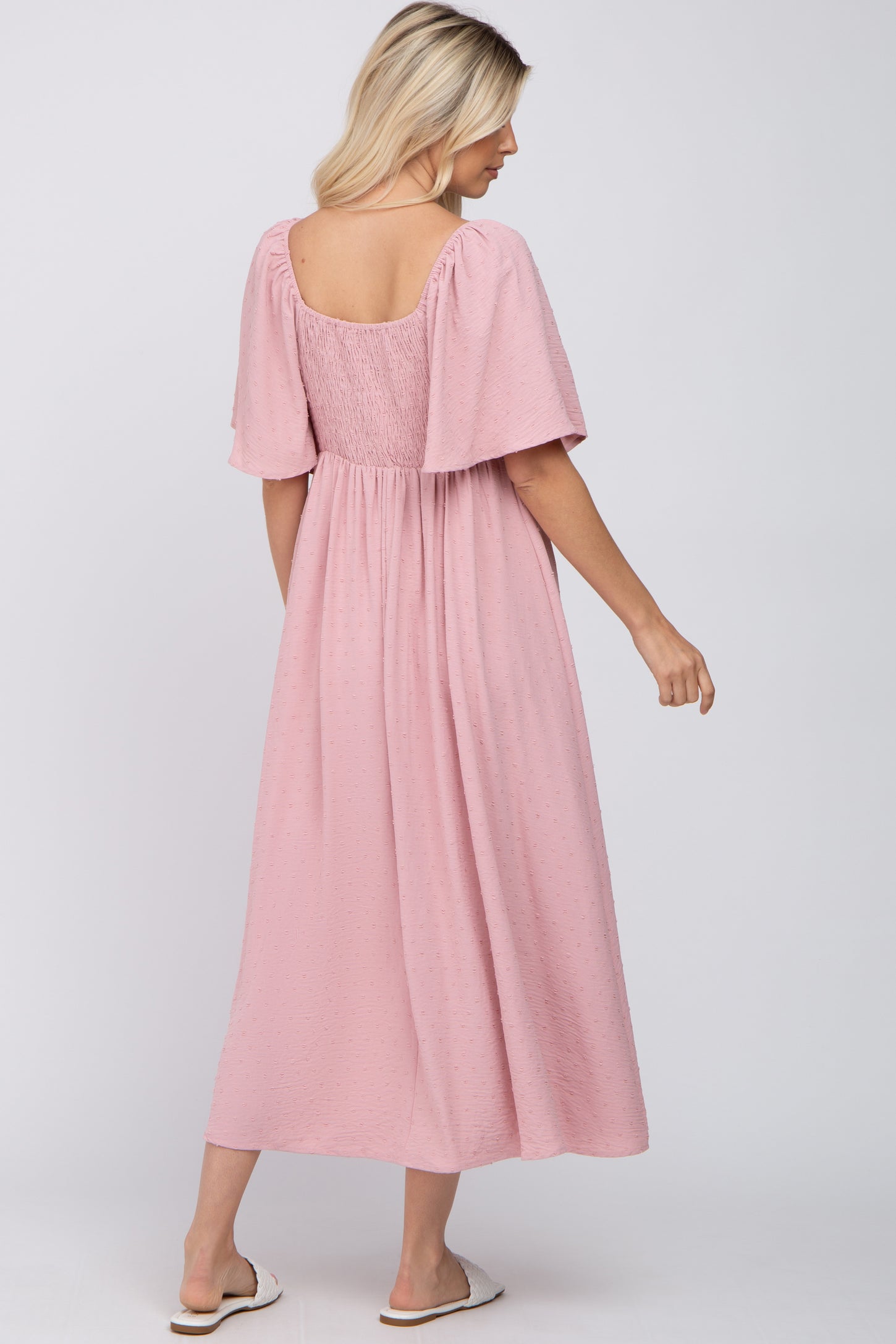 woman wearing a pink midi dress with short puff sleeves and a smocked back, standing sideways with a relaxed fit