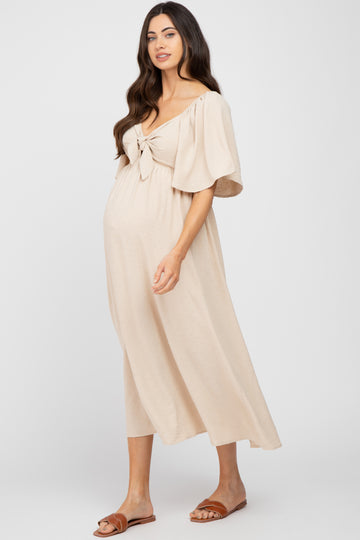 woman wearing a beige maternity dress with short sleeves and tie front detail, showing her baby bump