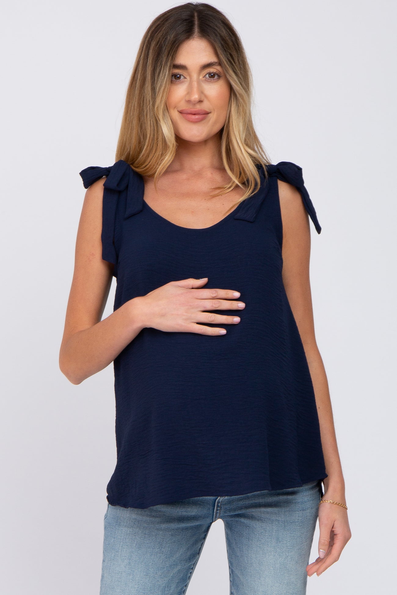 woman wearing a navy blue maternity top with tie shoulder details and holding her baby bump