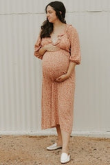 woman wearing a floral maternity dress with ruffles, cradling her visible baby bump