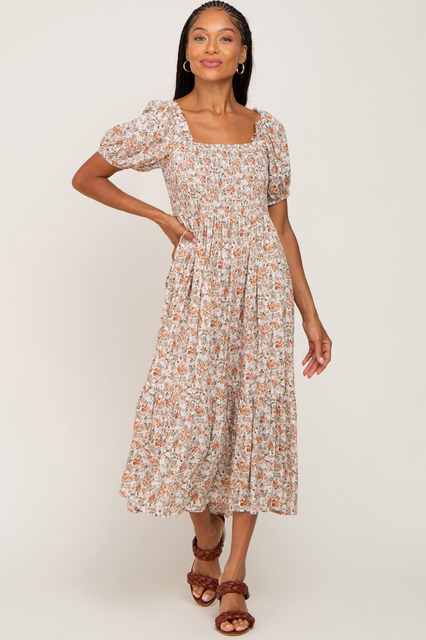 woman wearing a brown floral midi dress with puff sleeves and a square neckline, posing with one hand on her hip