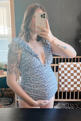 woman wearing a blue floral maternity swimsuit with ruffled sleeves and holding her baby bump