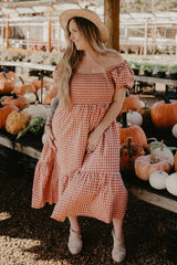 woman wearing a red and white gingham off-the-shoulder dress with puff sleeves, standing among pumpkins
