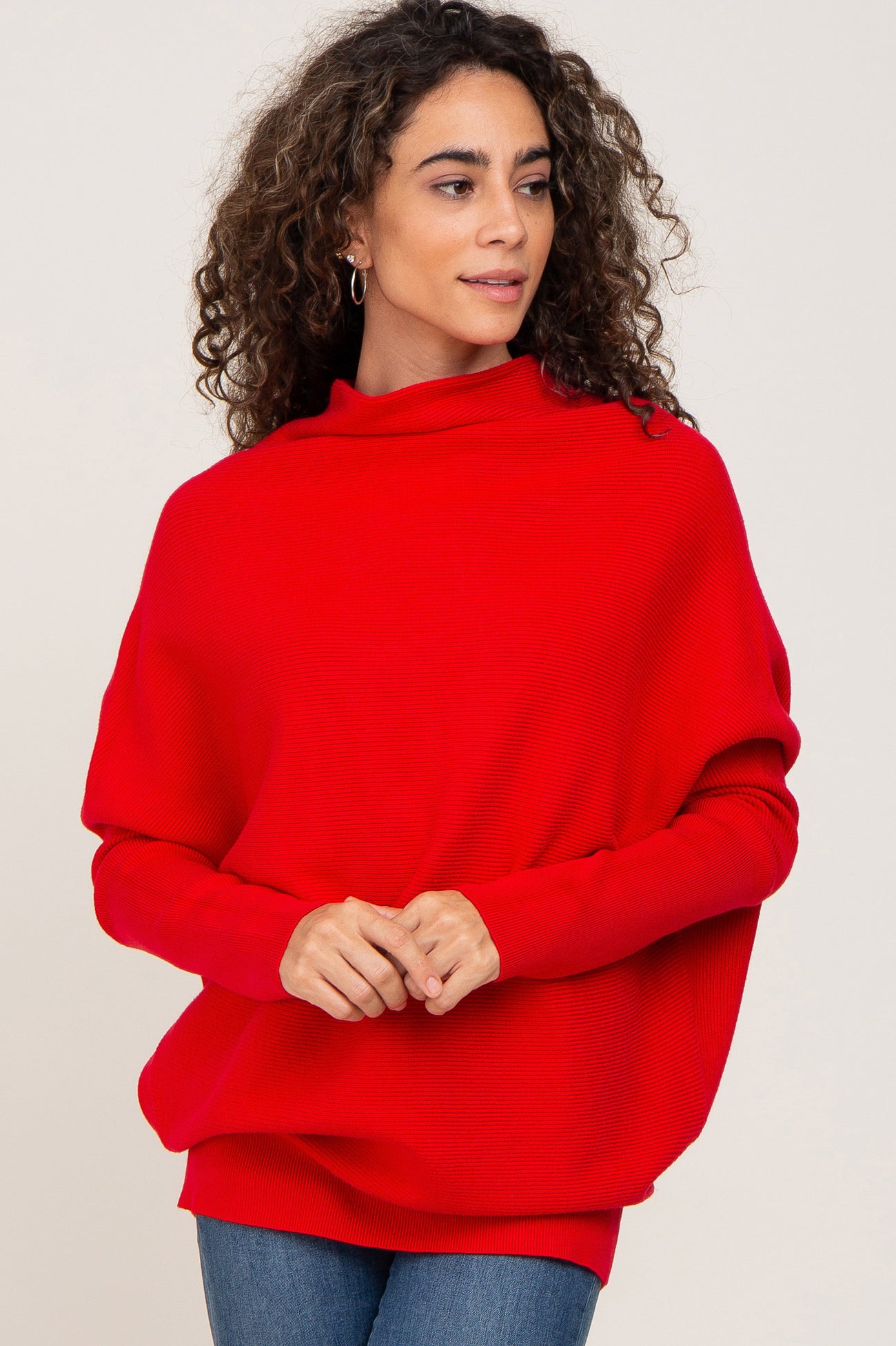 woman wearing a red oversized knit sweater with a high neckline and relaxed fit, styled with denim jeans