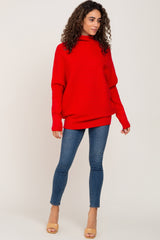 woman wearing a red oversized sweater with a high neckline and blue skinny jeans, standing in a neutral background