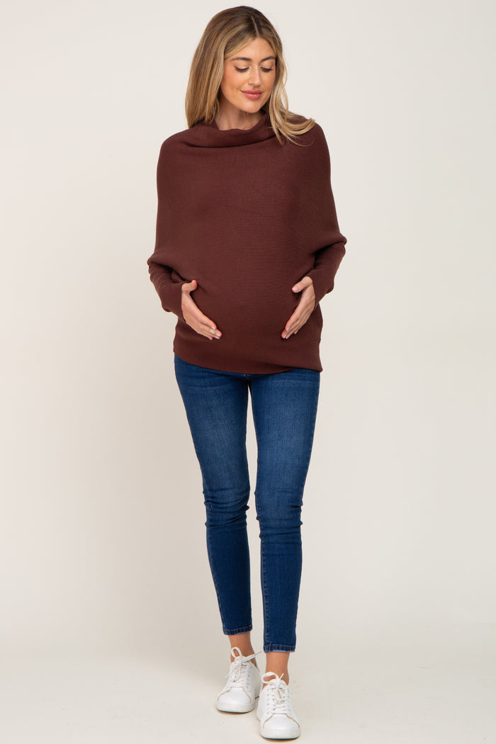 pregnant woman wearing a brown cowl neck maternity sweater and blue skinny jeans with white sneakers