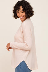 woman wearing a light pink waffle knit long sleeve top with a rounded hem and side slits, smiling and looking down