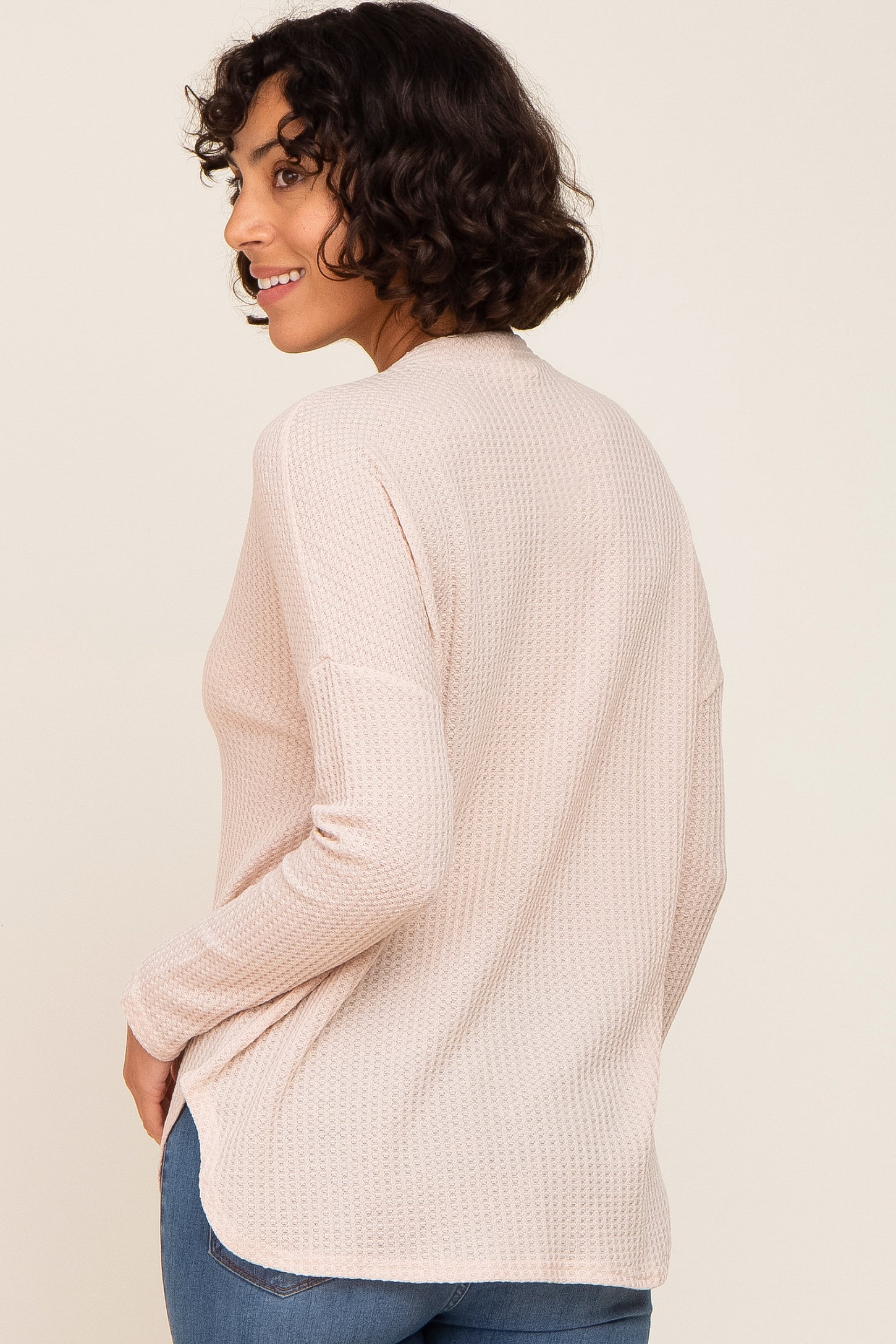 woman wearing a light pink long sleeve top with a textured pattern and a relaxed fit, turned slightly to the side