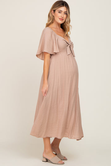 woman wearing a dusty pink maternity dress with a tie front and flutter sleeves, showing baby bump