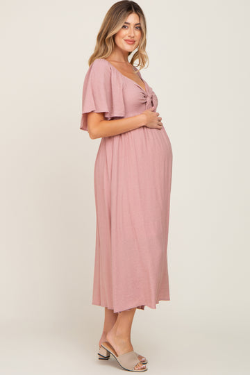 woman wearing a pink maternity dress with short flutter sleeves and a tie front, showcasing her baby bump