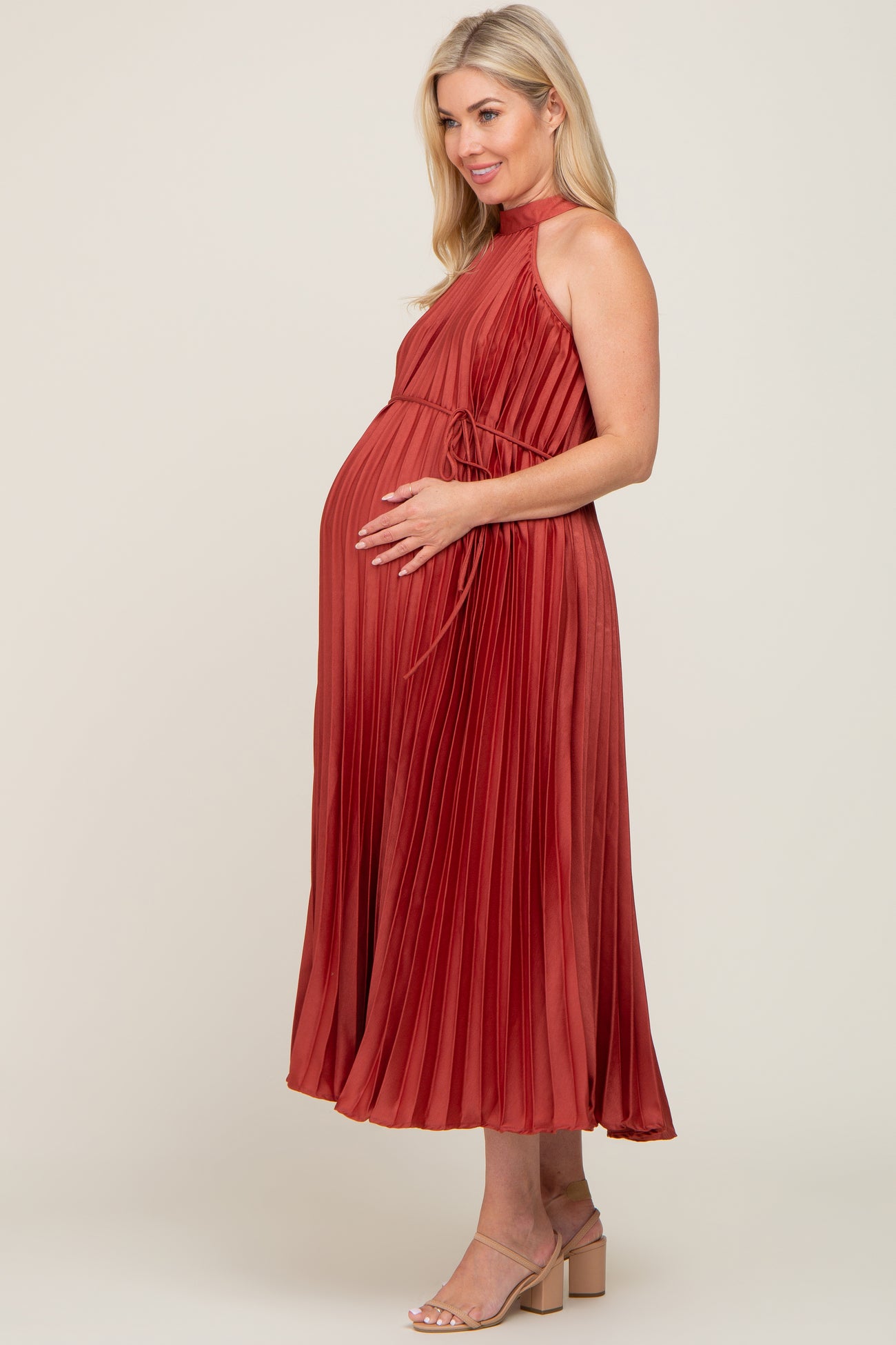 woman wearing a burnt orange pleated maternity dress with a tie waist and visible baby bump