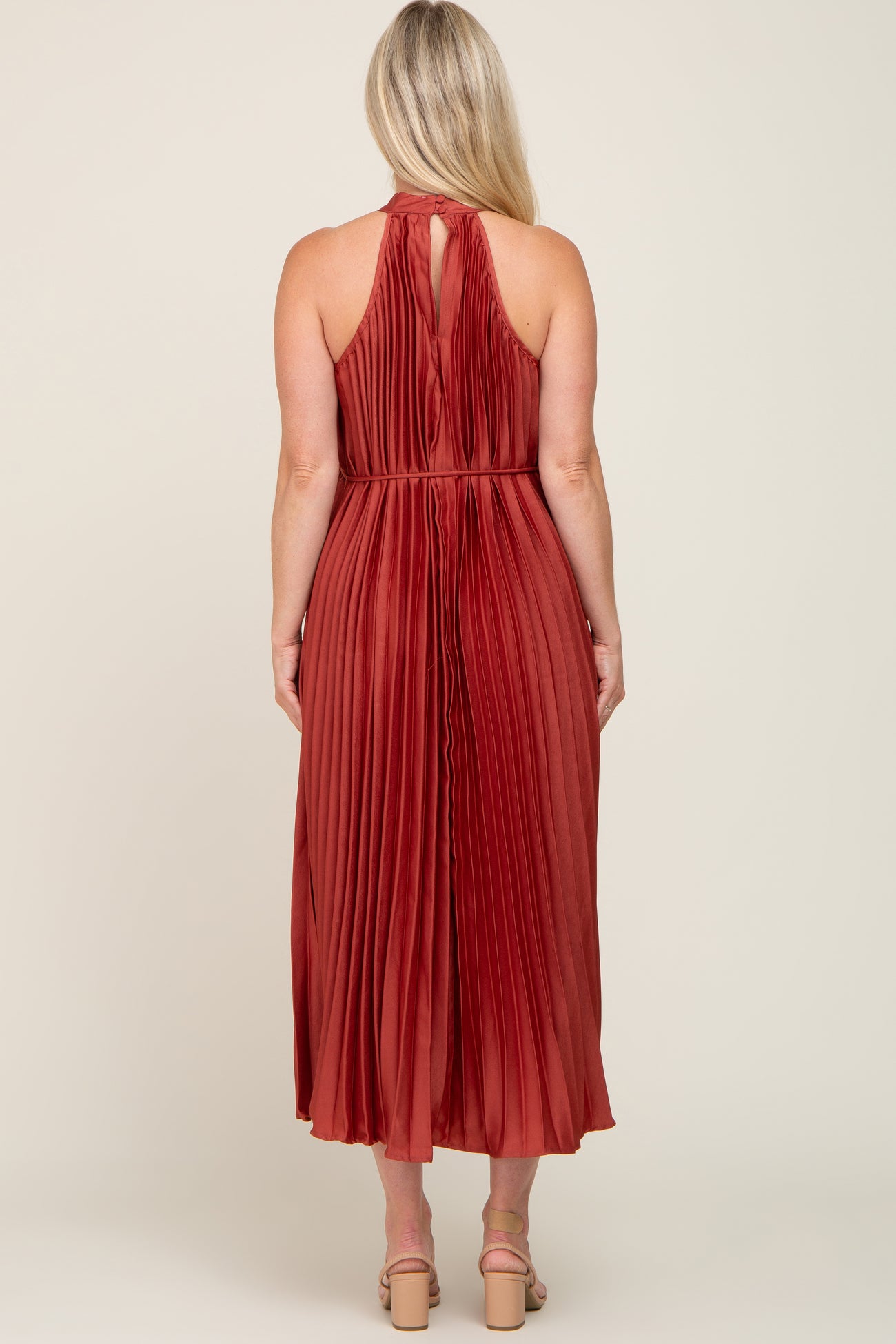 woman wearing a rust pleated maternity dress with a halter neckline and a back keyhole detail