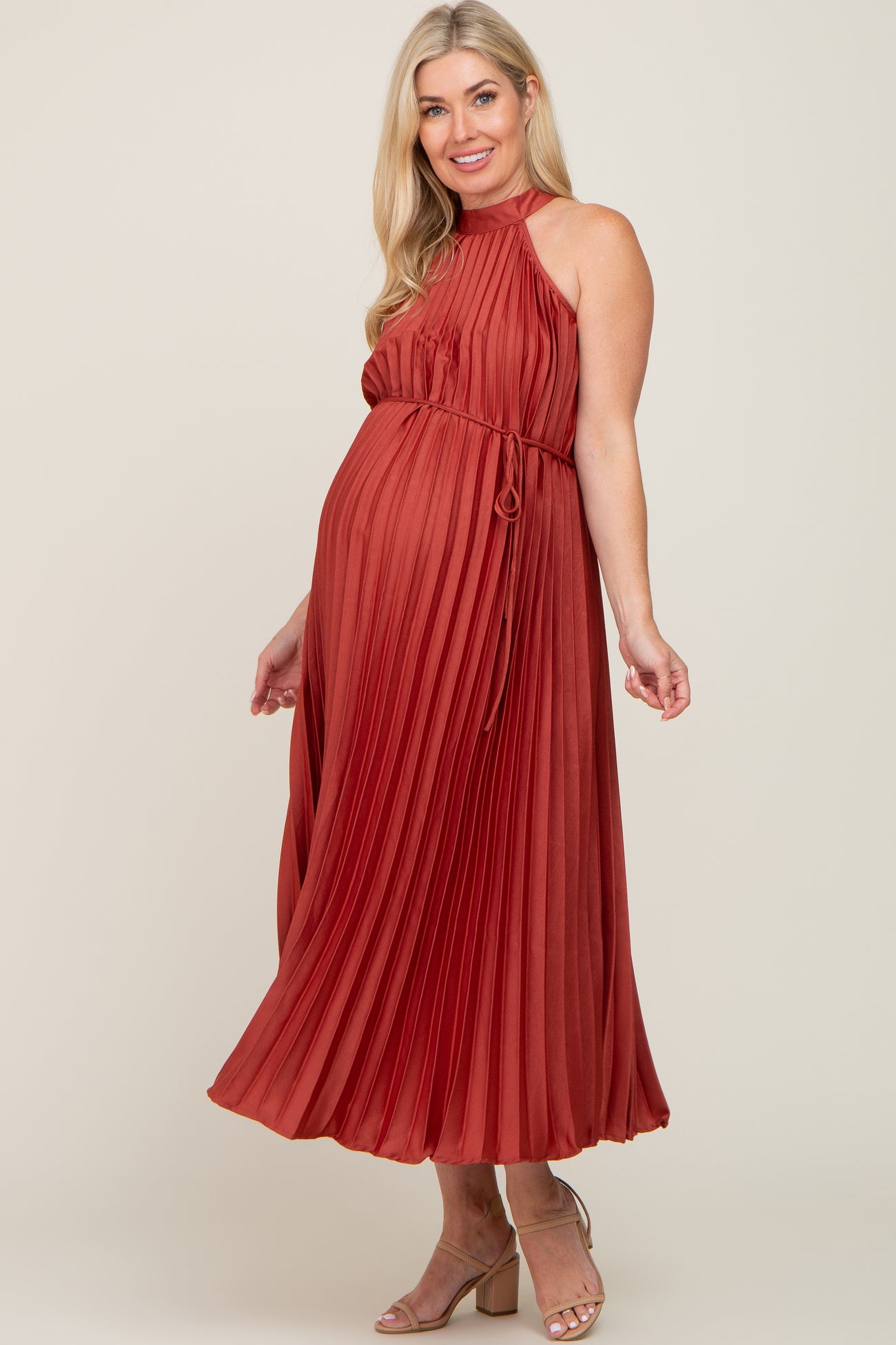 woman wearing a rust pleated maternity dress with a halter neck and tie waist, showing her baby bump