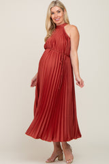 woman wearing a rust pleated maternity dress with a halter neck and tie waist, showing her baby bump