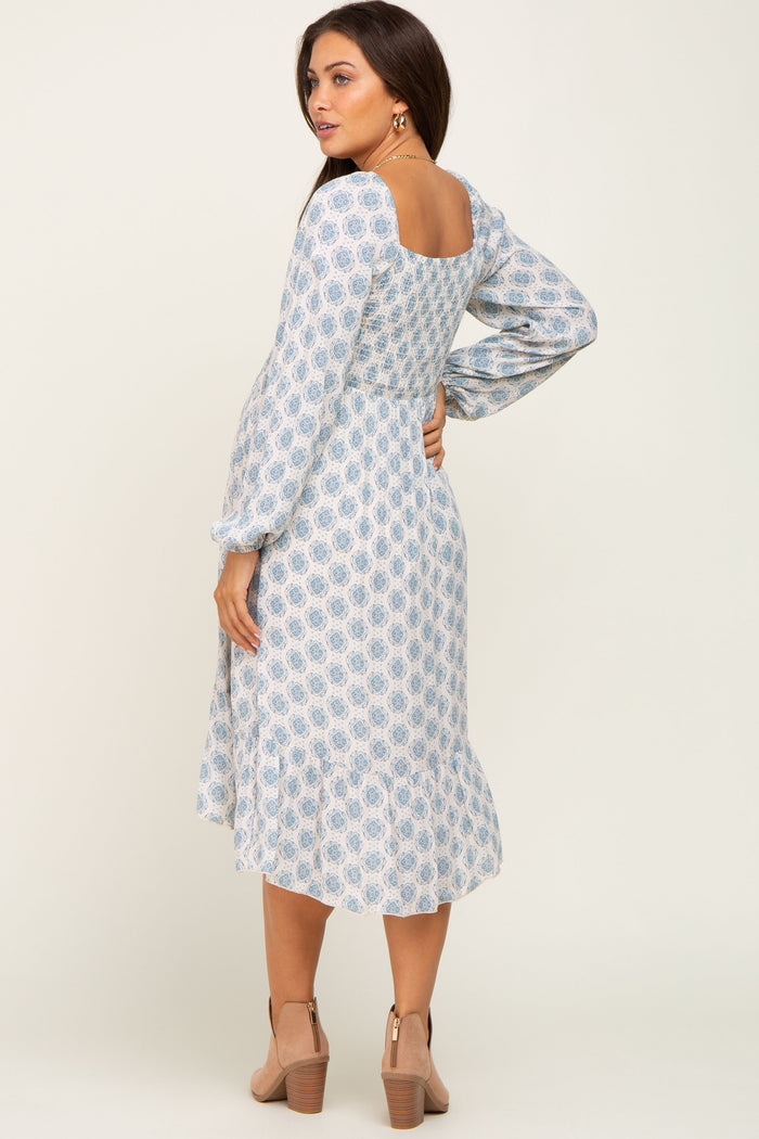 woman wearing a blue and white paisley print maternity midi dress with long sleeves and tan ankle boots