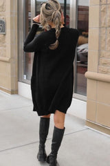 woman wearing a black oversized sweater dress with pockets and tall black boots, viewed from the back