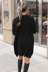 woman from behind wearing a long black cardigan sweater and black knee high boots on a sidewalk