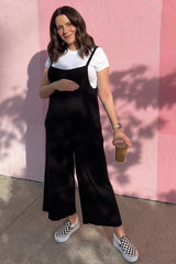 woman wearing a black maternity jumpsuit with a white t-shirt underneath, holding her baby bump and an iced drink