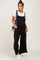 woman wearing a black maternity overall jumpsuit over a white t-shirt, styled with a small handbag and sneakers
