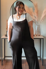 woman wearing a black maternity jumpsuit over a white t-shirt and smiling, with a baby bump visible