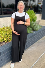 woman wearing a black maternity jumpsuit and holding her baby bump, standing outside beside greenery